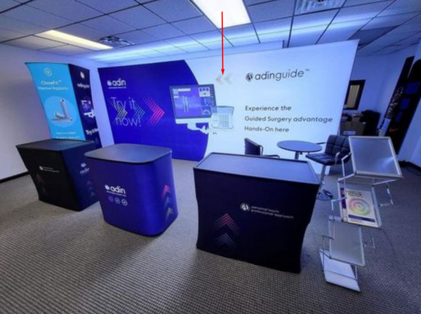 White Adinguide banner with blue-black interlocking arrows logo on 20ft backlit SEG light box wall