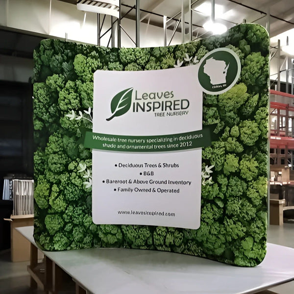 Green leafy backdrop with Leaves Inspired Tree Nursery sign on 8ft curved display