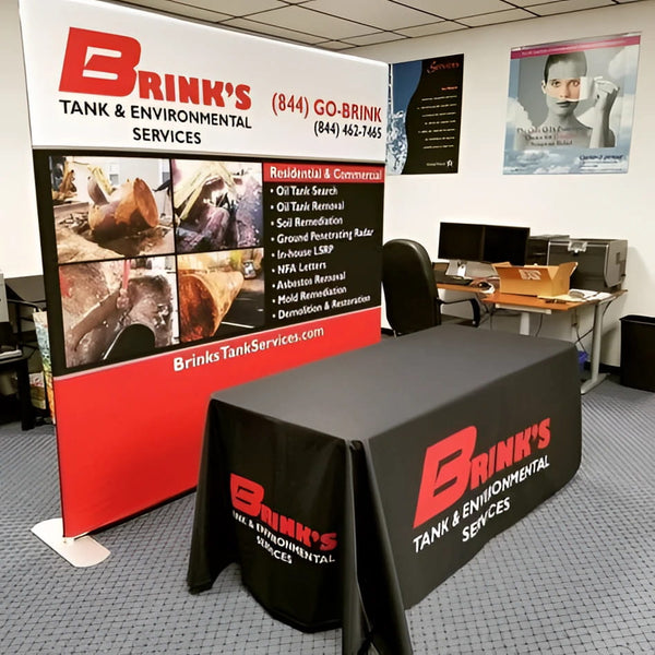 8ft straight tension fabric display with black tablecloth and Brinks Tank & Environmental Services logo