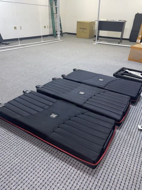 Black ribbed protective travel case with wheels, red trim, circular logo