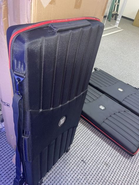 Black ribbed hard-shell wheeled travel case with red zipper and logo