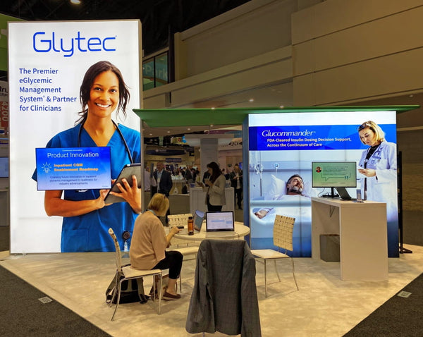 Glytec smiling woman in blue scrubs with tablet on Sync exhibit banner