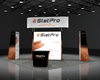 Sync 2-in-1 Backlit Hybrid Island Exhibit Kit E with black slatpro booth, orange and white branding, central screen, and vertical banners