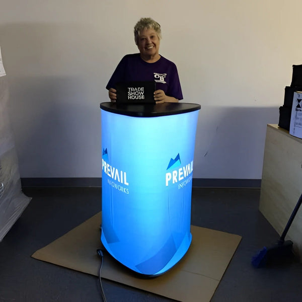 Blue illuminated cylindrical display table with Prevail Infoworks branding