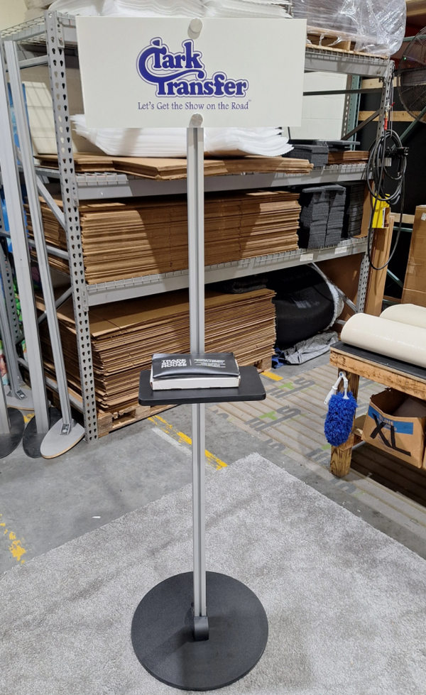 X1 Freestanding TV Monitor Stand with silver metal display, black base, and Clark Transfer sign