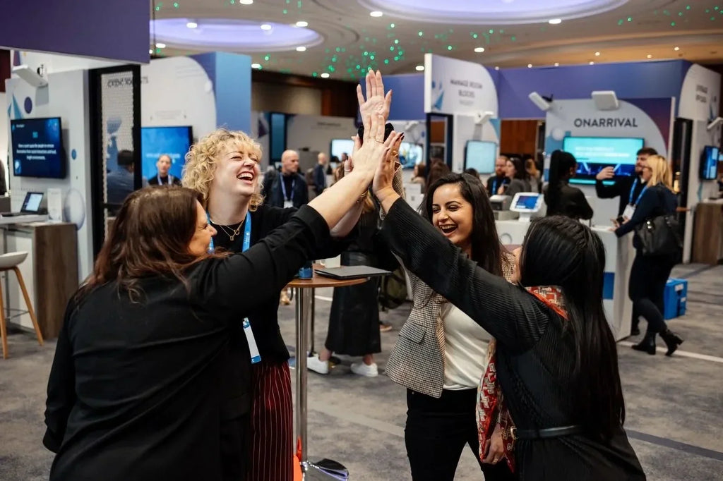 Four women high-five at tech trade show, boosting engagement