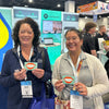 Two women at trade show booth holding light green cards with orange smiley mouths for 10x10 Frameless SEG Lightbox TV Display Kit 03
