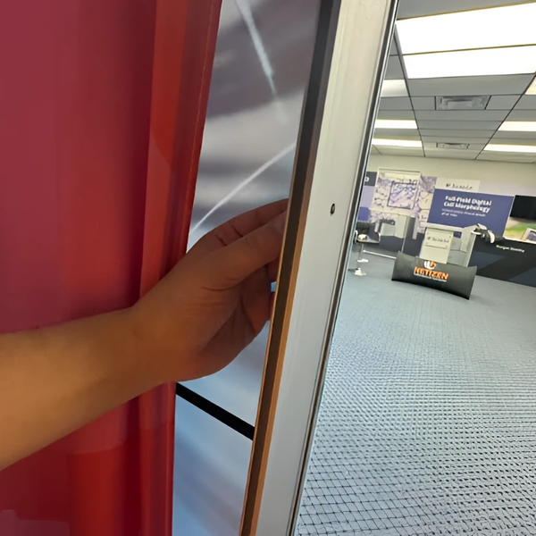 Hand holding red curtain edge for frameless lightbox wing nut display