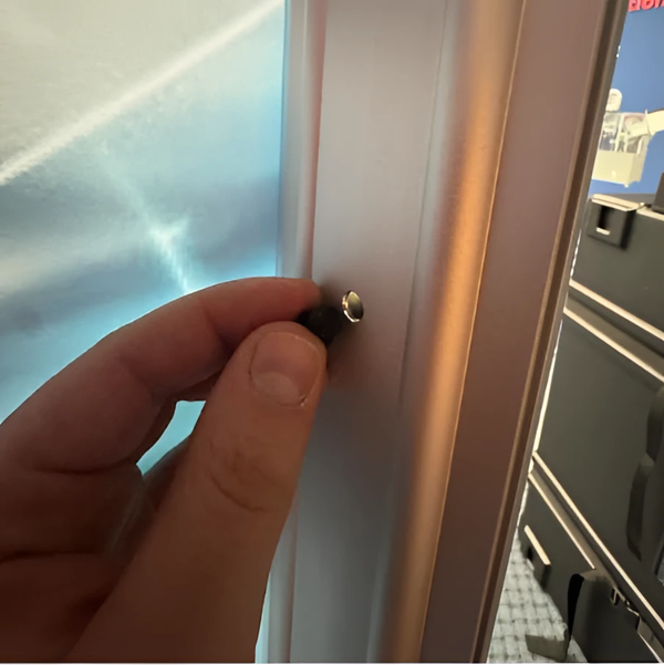 Hand holding silver-tipped black cylindrical connector for wing nut lightbox fasteners