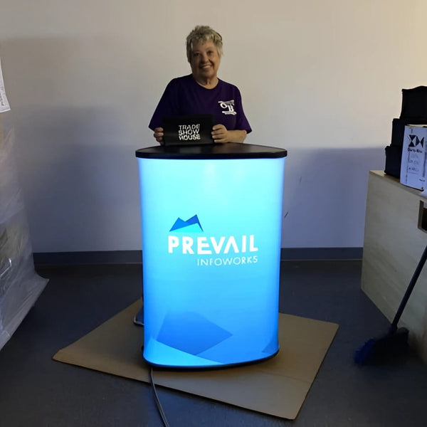 Blue illuminated cylindrical display stand with Prevail Infoworks logo